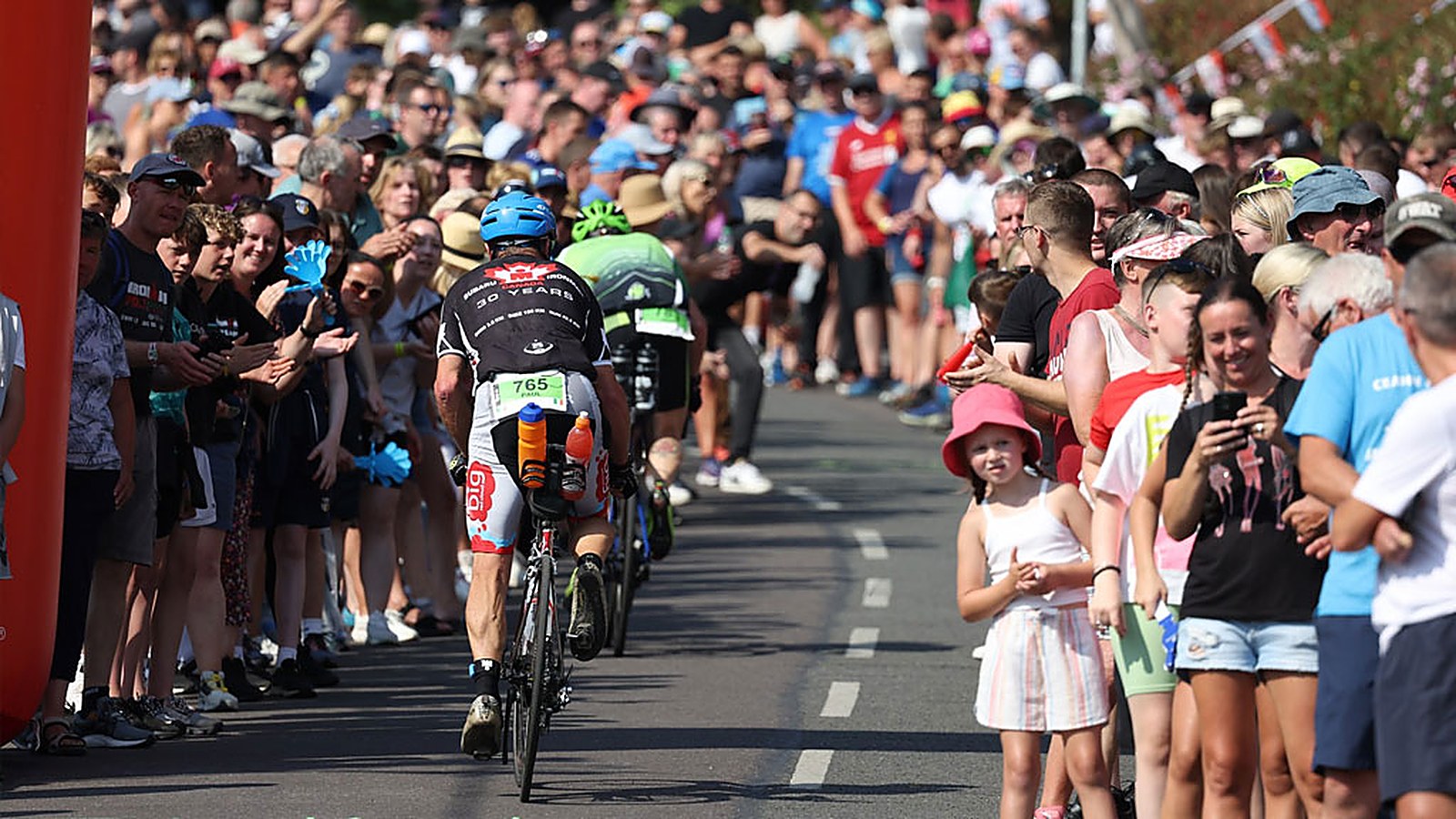 Family and friends cheering for athletes from the barrier, a young girl in a pink hat watching, during race week
